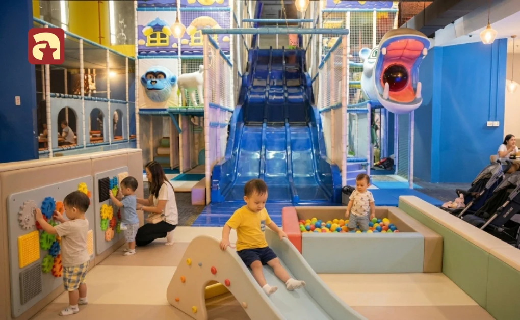Toddlers playing on small slide and ball pit with large blue multi lane slide at Amazonia indoor playground in Singapore