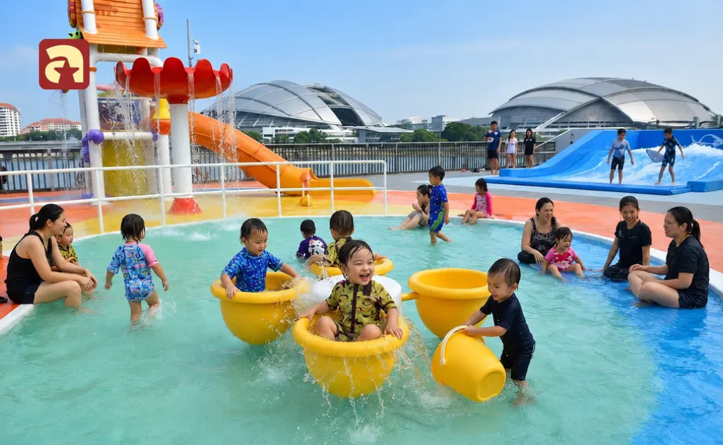 Toddlers playing and splashing in the shallow pool and yellow bucket seats at Splash N Surf rooftop water park in Singapore