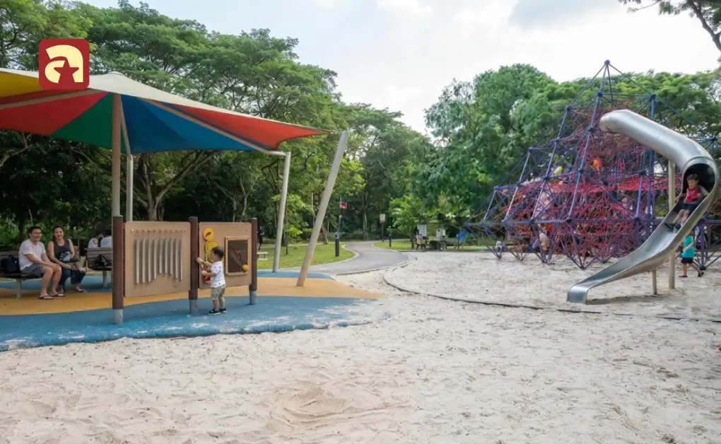 Toddler exploring percussion wall near sandy play area and large pyramid climbing net at West Coast Park Adventure Playground Singapore